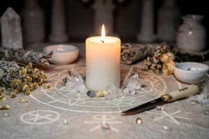 Vela blanca encendida en un altar decorado con cristales y hierbas aromáticas para rituales de protección espiritual.