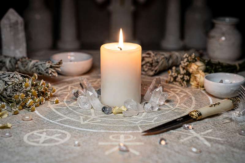 Vela blanca encendida en un altar decorado con cristales y hierbas aromáticas para rituales de protección espiritual.