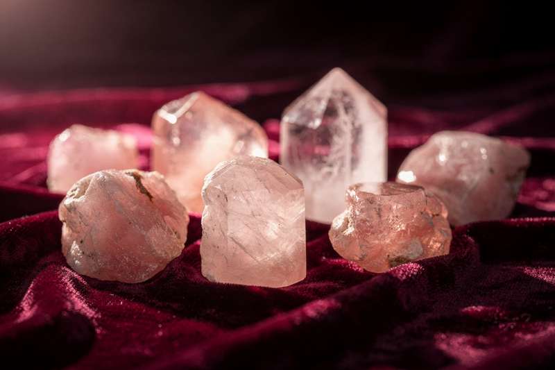 Cuarzo rosa pulido junto a otras piedras de tonalidades cálidas sobre una superficie reflectante.