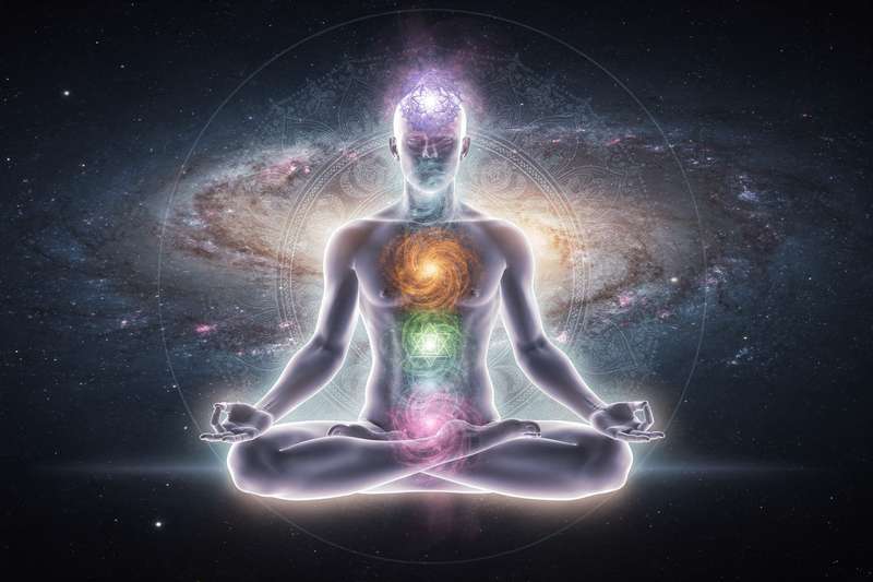 Persona en posición de loto meditando con visualización de los siete chakras alineados verticalmente en el cuerpo.