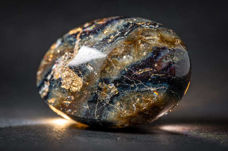Cristal marrón y azul de Pietersite con vetas características que reflejan luz dorada intensamente.